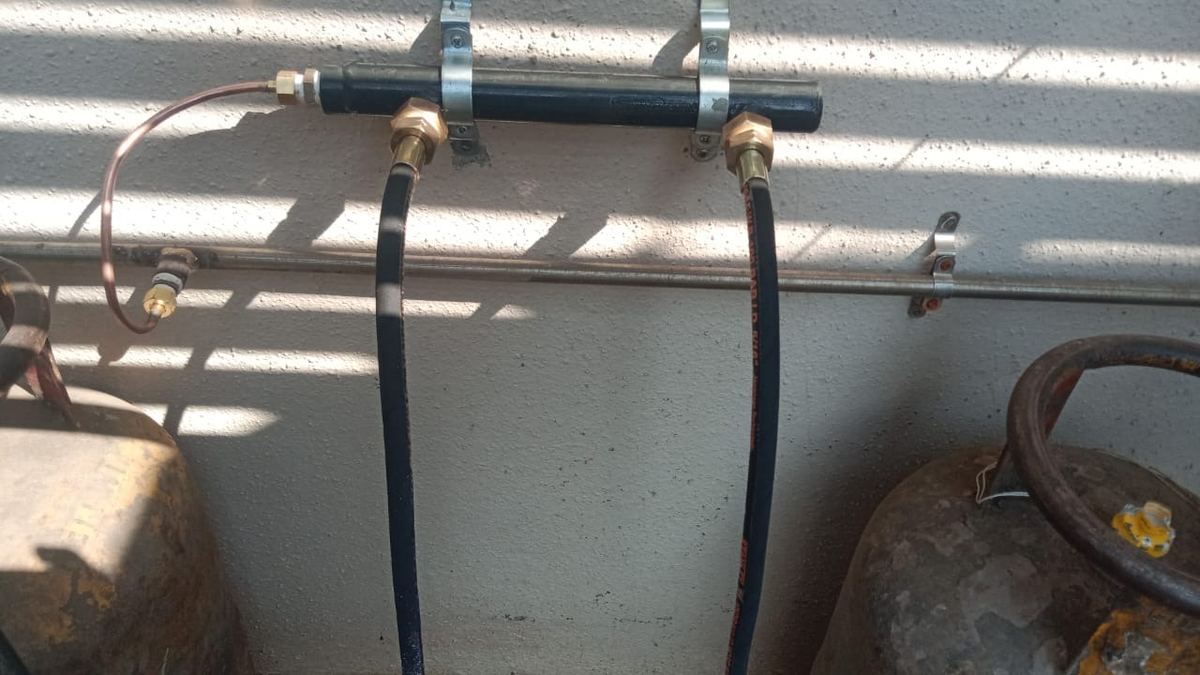 Two LPG cylinders joined to a wall-mounted steel header with copper and hose connections